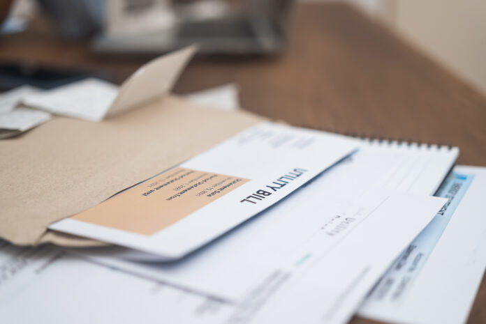 Utility bill statement details, displaying due amount, alongside a phone calculator, set on a wooden apartment table. Financial responsibility in focus.